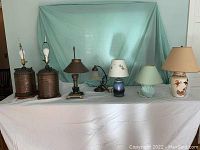 Full view of the set of six lamps including two table lamps with metal canister bases, vintage arched lamp with glass shade, various ceramic and metal base table lamps, and floor lamp.