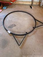 Photo showing metal circular log holder on barn floor, visible three triangular support legs.