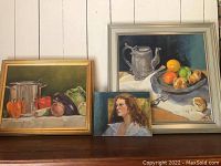 Three framed paintings by Nancy Armstrong displayed together on a ledge. Shows the entire lot for overall context.