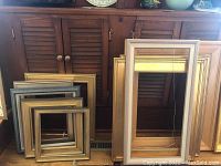 Two large rectangular frames leaning against cabinet with stacked square frames to left