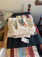 Patchwork quilt on bed with folded pile of white and cream linens including crochet pieces on top