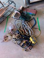 Photo of 4 belt and 6 disc bench sander with pile of ropes, cords, and tools on floor next to it.