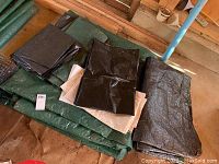 Photo showing stacked tarps including large green, black and beige folded tarps in a barn setting.