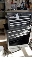 Craftsman black tool chest stacked on a rolling tool cart inside workshop, showing condition and relative size of both units.