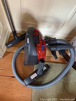 Red Miele vacuum cleaner body with flexible hose and black power nozzle, placed on wooden floor with green carpet patch.