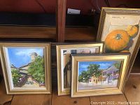 Five framed paintings stacked together showing variety of subjects and gold-toned frames.