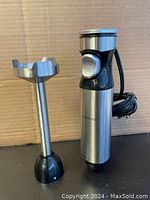 Two-part immersion hand blender: motor unit and detachable blending shaft with stainless steel blades, placed upright against cardboard background