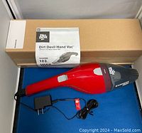 Photo of the complete set including the red cordless vacuum, charger cord, user manual, and original packaging box.
