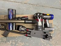 Top-down view of vacuum handheld unit, wand, cleaner heads, tools, charger and docking station on box