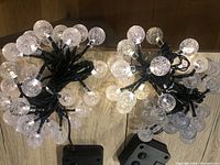 Two coiled solar globe string light sets showing clear bubble-effect globes with LED lights attached to black wiring, laid on wooden floor.