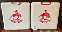 Pair of white seat cushions side by side, both featuring red Ottawa Rough Riders logo and red handles.