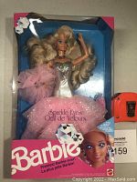 Full front view of Barbie Sparkle Eyes doll in original unopened box with pink glittery skirt and silver outfit visible.