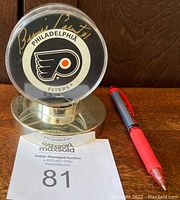 Signed Philadelphia Flyers hockey puck encased in custom clear plastic holder with silver base, showing bold gold signature of Bernie Parent.