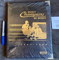 Front of the sealed black binder with gold hockey player graphics and text 'Hockey Champions Du Hockey 1993-1994' with Kraft logo.