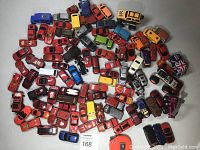 Top-down view of approximately 70 diecast cars and trucks spread on a flat surface, mostly red sports cars with some vans and monster trucks.