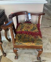 Front view of the antique corner chair showing the carved wooden arms, upholstered seat, and pillow.