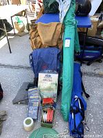 Full lot arranged outside showing green Sport-Brella umbrella, blue camping chair bag, brown backpack, packaged utility tarp, and small camping accessories.