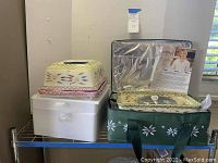 Photo showing covered butter dish on top of pink floral tray and Styrofoam packaging, next to green insulated carrying bag containing another ceramic piece with instructions