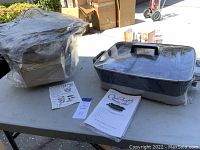 Electric skillet and covered roaster chafing dish on table with instruction manuals, both new in box.