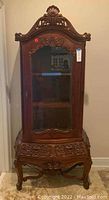 Front view showing decorative carved wooden curio cabinet with glass door and two drawers at the base.
