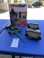 DynaTrap insect trap new in box with two green sprinkler spikes and two white-gray sprinkler hose connectors displayed on a blue table outdoors.