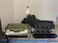 Full view of the George Foreman grilling machine with all assorted removable plates shown around it, including waffle, sandwich, baking, and long grill plates.