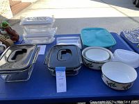 Overview showing multiple Lock & Lock glass containers with black locking lids, ceramic casseroles with Christmas motif, blue plastic lid, and white storage bags on a blue table.