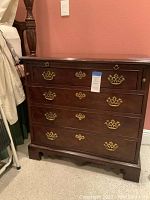 Front view of nightstand showing four drawers with brass bail pulls and scalloped base