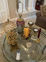 Overview of all home decor items on glass table including lamp, metal sphere sculptures, assorted candles and candle holders