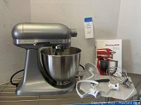 Front view of KitchenAid Artisan Mini stand mixer with stainless steel bowl and attachments displayed