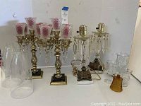 Full view of two ornate brass candelabras, two clear glass lamp bases with decorative metal bases, various clear etched glass shades, and some glass candlestick holders.