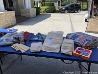 View of all items including new beige towels of different sizes on blue table, NFL sleeping bag rolled up, cleaning liquid bottle, and Scrub Daddy scrubbers.