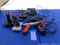 Overall view showing Sega Genesis console with multiple joystick controllers and Nintendo Zapper on blue table.