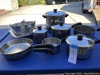 Full set of RevereWare pans including stockpot, saucepans, fry pans, Bundt pan, and roaster pan arranged on a blue table outdoors.