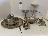 Overview of all silver plate serving pieces on table showing trays, goblets, spoon, serving stand, toast rack, and condiment jar.