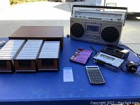 Full lot showing Sony boom box, Panasonic cassette player, HP calculator, and wooden cassette tape organizer with tapes.