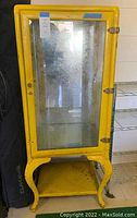 Front view of yellow metal cabinet with glass door and mirror interior