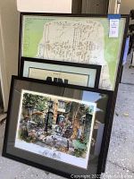 Two framed art prints leaning against a wall, one showing a family tree and the other an outdoor café scene.