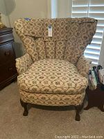 Full front angle of the wingback chair revealing floral pattern upholstery and wood legs.