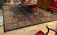 Full view of large wool area rug under dining table with detailed classical design in black and earth tones.