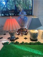 Full view of two lamps and large ginger jar with stand on black and white tile floor near window