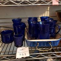 Photo showing the blue enameled cast iron baking dish with several blue glasses arranged inside and next to it on a metal shelving unit.