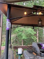 View of canopy corner showing steel post, canvas top, globe string lights and partial view of grill area