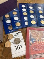 Multiple Presidential $1 Coin Collections in blue folders spread on table with some loose coins including Eisenhower dollars.