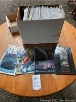 Photo of a large cardboard box filled with numerous comic books in plastic sleeves arranged on a table with a few comic covers visible in front including Wolverine and Space Above and Beyond.