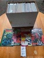 Long cardboard box filled with clear-bagged comics and four front-cover issues displayed on table