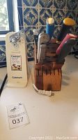 Cuisinart electric can opener next to wooden knife block with knives of varying handle colors.