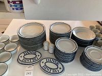 Stacks of dinner plates, salad plates, soup bowls, dessert plates alongside salt & pepper shakers and two oval Dansk Bistro trivets