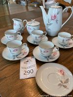 Full display of Noritake Rosemarie tea set with teapot, sugar bowl, cream pitcher, cups and saucers on wooden table.