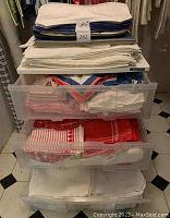 Top view of stacked white and blue cloth placemats on top of the storage unit with folded linens inside drawers.